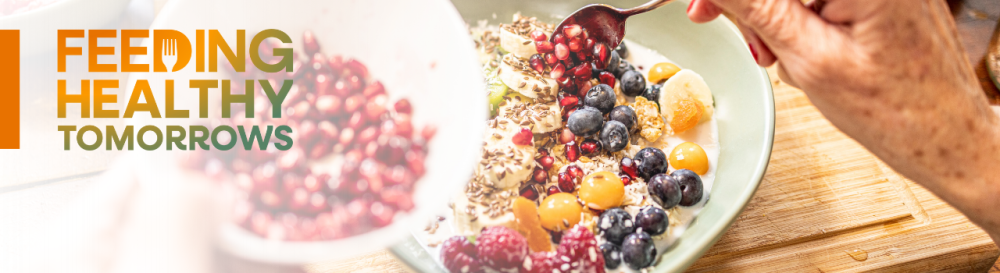 A bowl filled with yogurt with blueberries, pomegranate, rasberries and granola text that reads feeding healthy tomorrows in top left corner