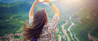 Woman on a hilltop making a heart shap with her hands over a majestic view