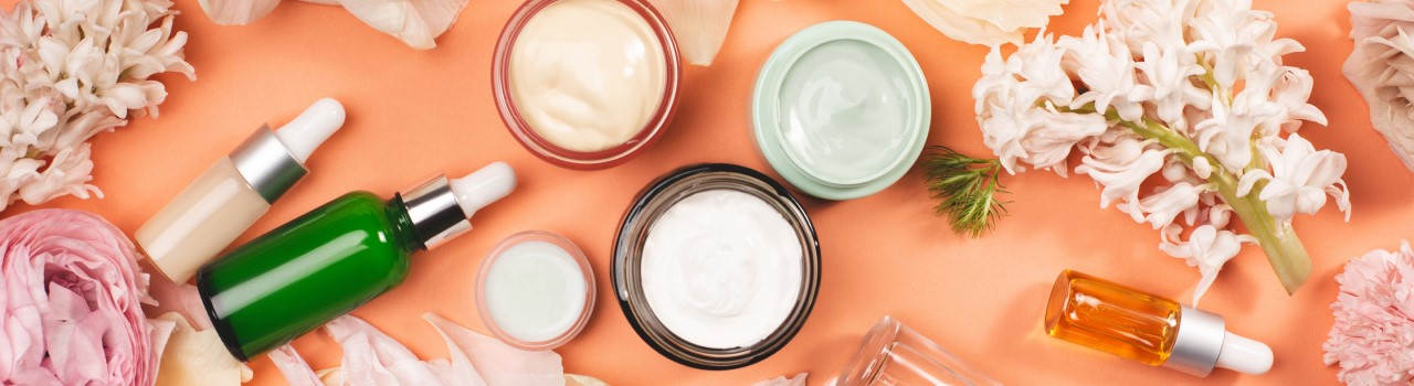 Beauty products displayed on a salmon colored table top surrounded by white flowers
