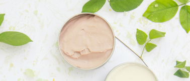 Blue light skincare products sit on a marble table top surrounded by green leaves